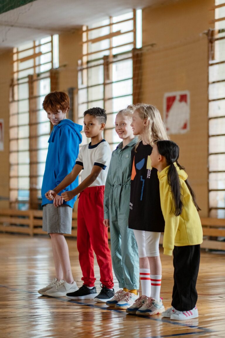 Grupa dzieci w strojach sportowych na sali gimnastycznej przed lekcją WF