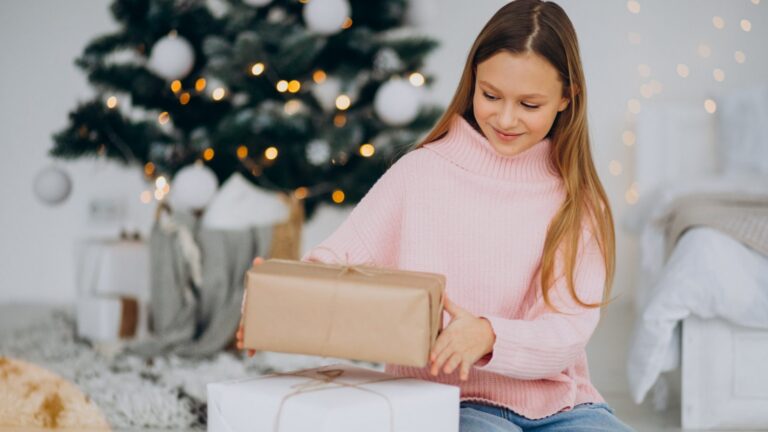 Nastoletnia dziewczynka w różowym swetrze trzyma prezent przy choince